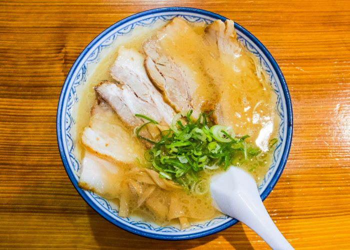 A top-down shot of tonkotsu ramen, showing a spoon resting in a thick broth,